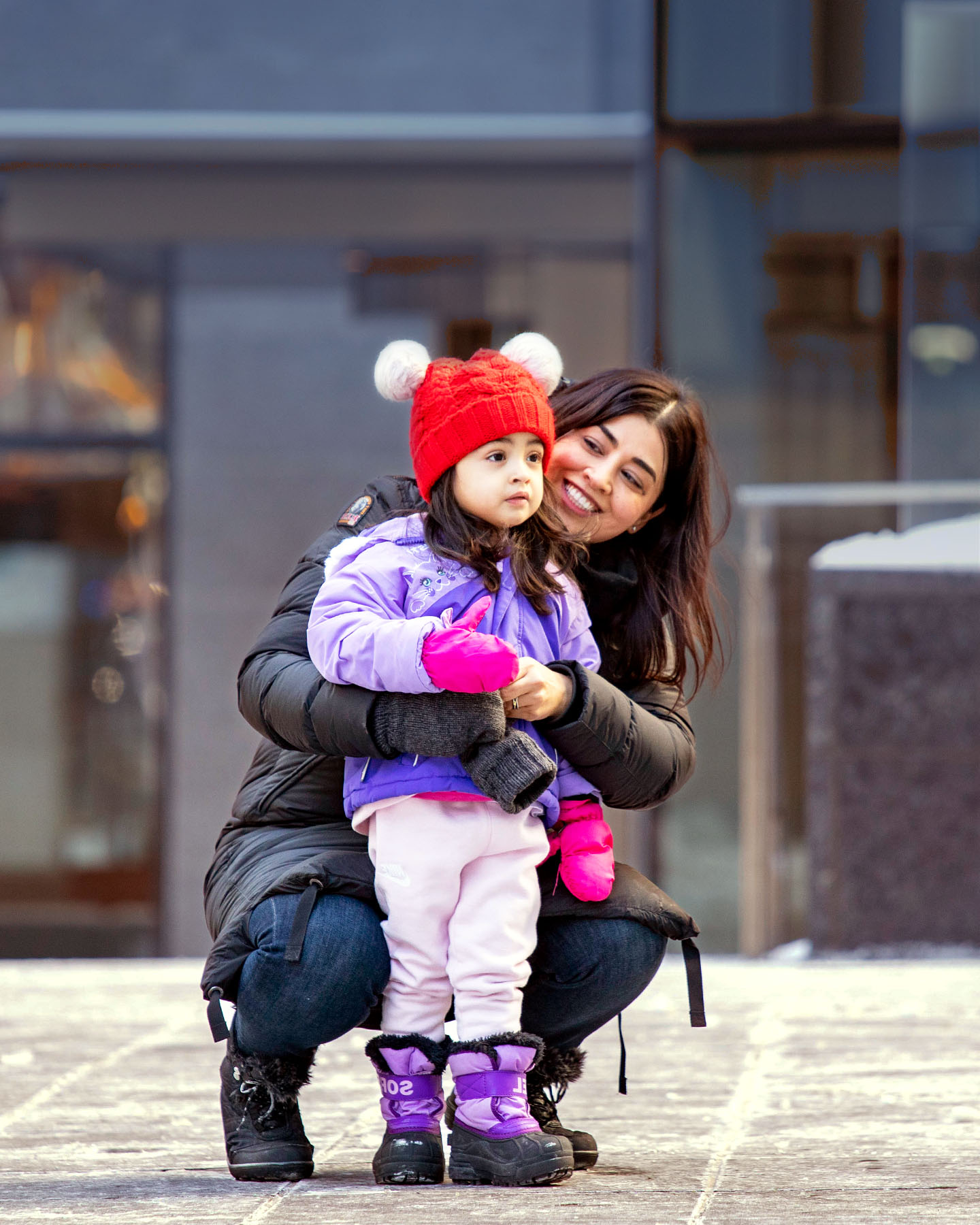Picture of a mother and a girl in front of a building wearing jackets